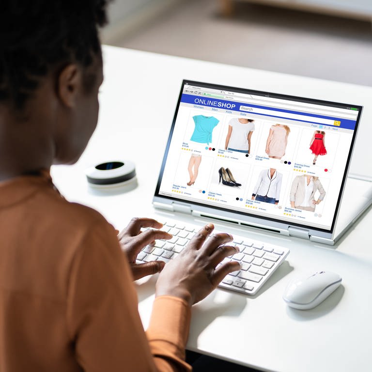 Eine junge Frau sitzt vor ihrem Laptop und schaut sich in einem Onlineshop Klamotten an (Symbolfoto)