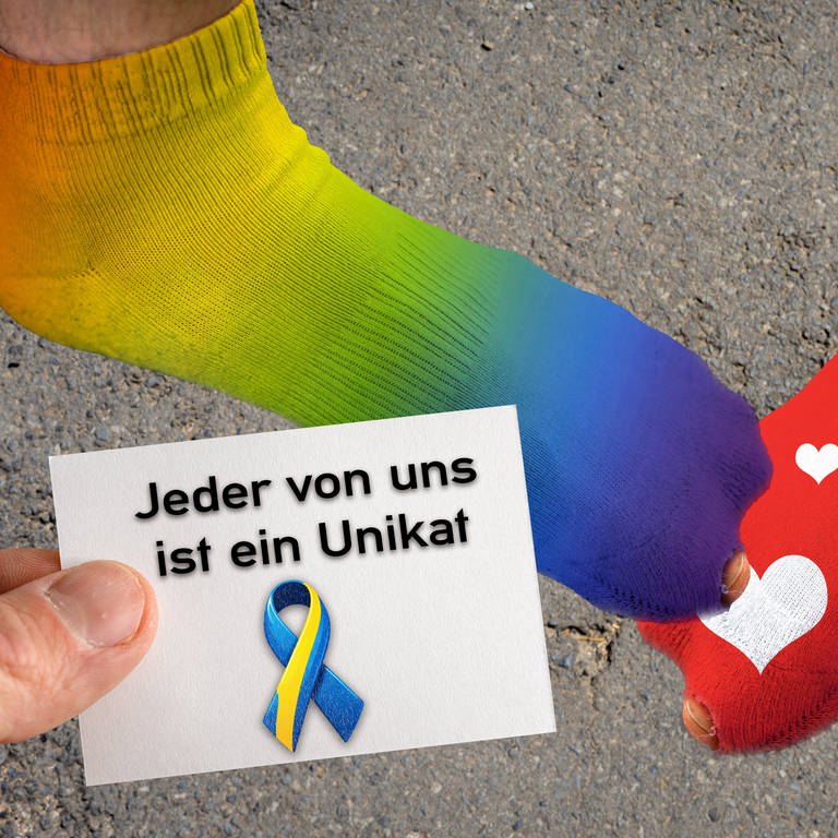Symbolbild Welt Down Syndrom Tag, Zwei Füße mit verschieden farbigen Socken und eine Hand mit einem Stück Papier mit der Aufschrift: Jeder von uns ist ein Unikat. FOTOMONTAGE
