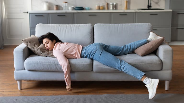 SYMBOLBILD: Eine Frau in rosa Bluse und Jeans liegt erschöpft auf der Couch.