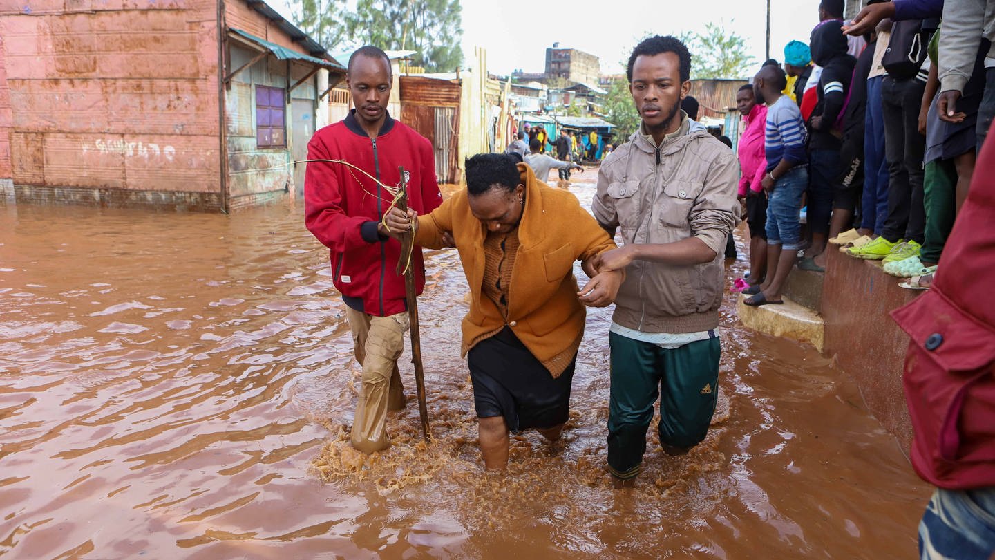 IMAGO / Xinhua (Foto: IMAGO, Anwohner helfen einer Frau während Überschwemmungen nach heftigen Regenfällen in den Armenvierteln von Mathare in Nairobi, Kenia)