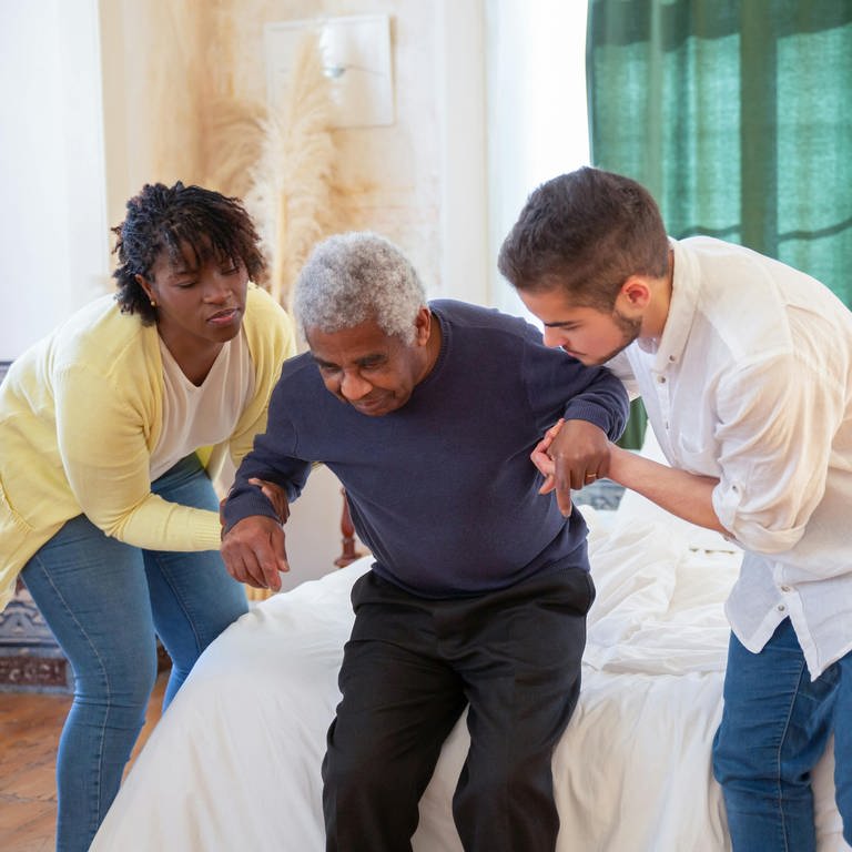 Zwei Altenpfleger helfen einem Mann beim Aufstehen