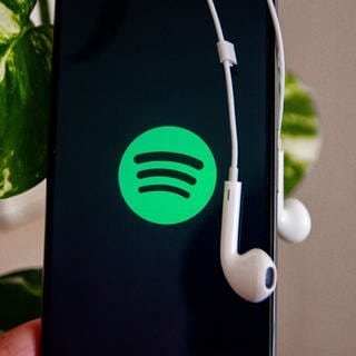 Ein Handy zeigt das Spotify-Logo. Über dem Gerät hängen Kopfhörer.