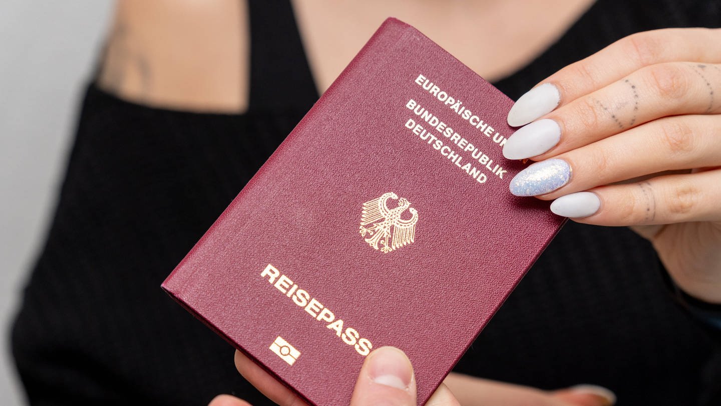 Mann gibt einer Frau einen deutschen Reisepass (Symbolbild) (Foto: IMAGO, IMAGO / Bihlmayerfotografie)