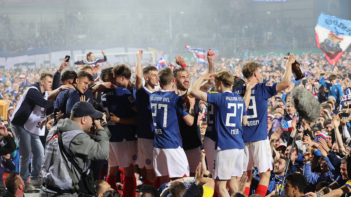 Spieler von Holstein Kiel feiern mit den Fans im Stadion den ersten Aufstieg in die Fußball Bundesliga. (Foto: IMAGO, IMAGO / Susanne Hübner)