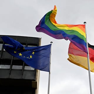 Eine Regenbogenflagge weht neben einer Deutschlandflagge und einer Europaflagge