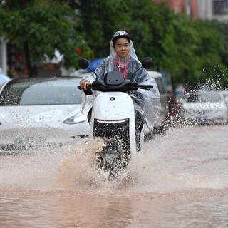 Eine Frau fährt mit ihrem Roller über eine überflutete Straße.