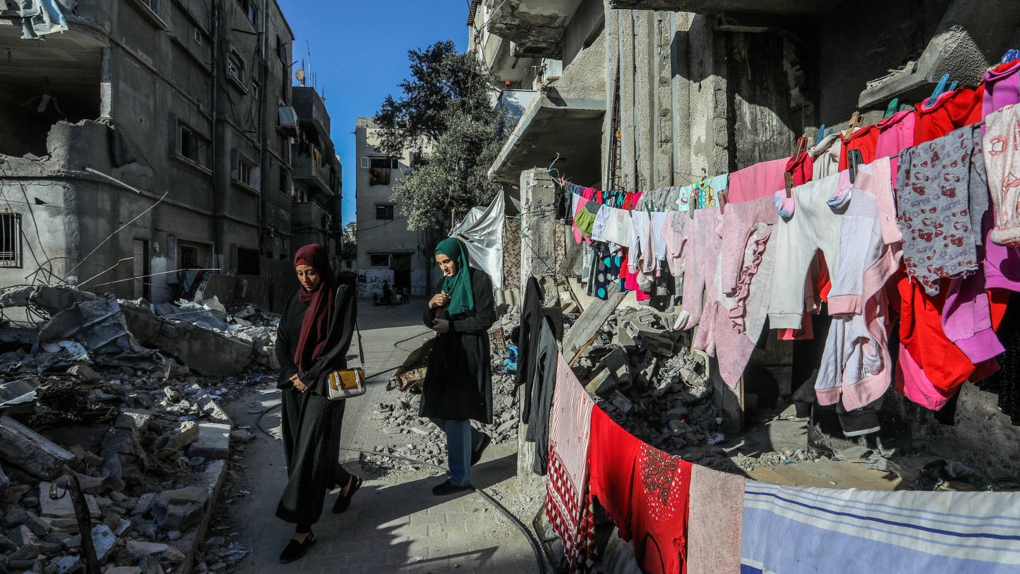 Vertriebene Palästinenserinnen aus der Stadt Rafah, die vor den Kämpfen fliehen, gehen während der anhaltenden Kämpfe zwischen Israel und der Hamas an einem von israelischen Kampfflugzeugen zerstörten Gebäude vorbei. (Foto: dpa Bildfunk, picture alliance/dpa | Abed Rahim Khatib)
