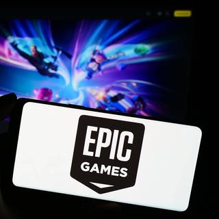 Ein Smartphone mit dem Logo von Epic Games vor einem Bildschirm, auf dem Fortnite läuft.