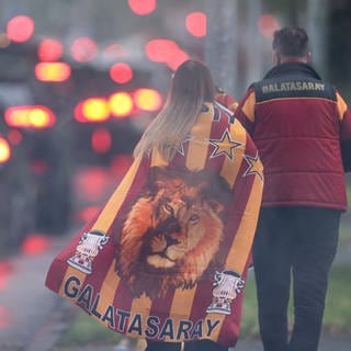 Ein Paar gekleidet in den Farben des türkischen Meisters Galatasaray Istanbul läuft über die Straße. - Bei der Meisterfeier in Stuttgart wurden auf dem Schlossplatz 18 Leute festgenommen.
