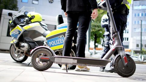 Ein E-Scooter steht vor einem Polizeimotorrad. (Foto: dpa Bildfunk, picture alliance/dpa | Martin Gerten)