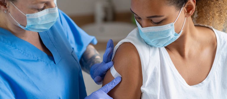 Junge Frau bekommt nach dem Impfen ein Plaster aufgeklebt (Foto: IMAGO, IMAGO / Westend61)