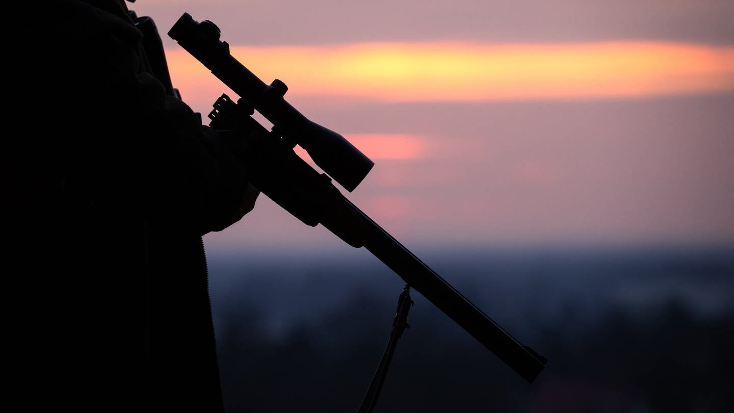 Ein Jäger hält sein Gewehr in der Abenddämmerung
