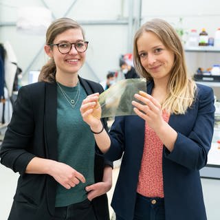 Johanna Baare (l) und Anne Lamp von Traceless Materials zeigen eine Folie aus abbaubaren Materialen. (Foto: picture-alliance / Reportdienste, picture alliance/dpa | Philipp Schulze)